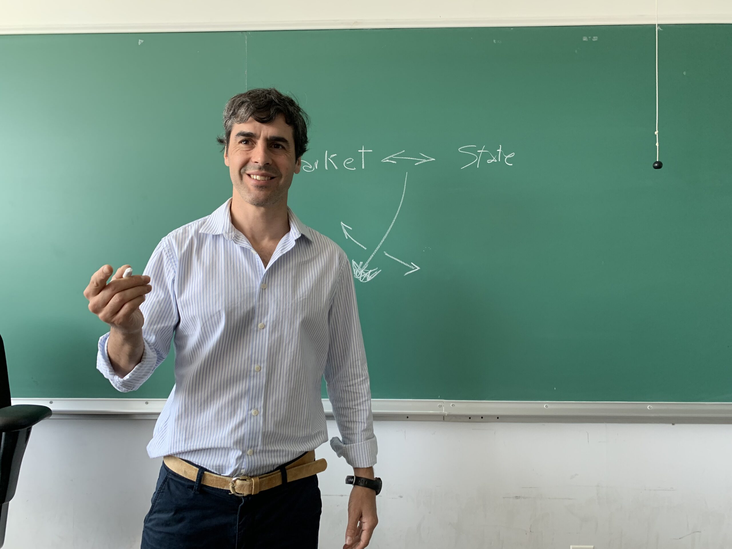 A picture of Juan Ferre standing in front of a chalkboard, a piece of chalk in his hand. He appears to be mid-teaching.